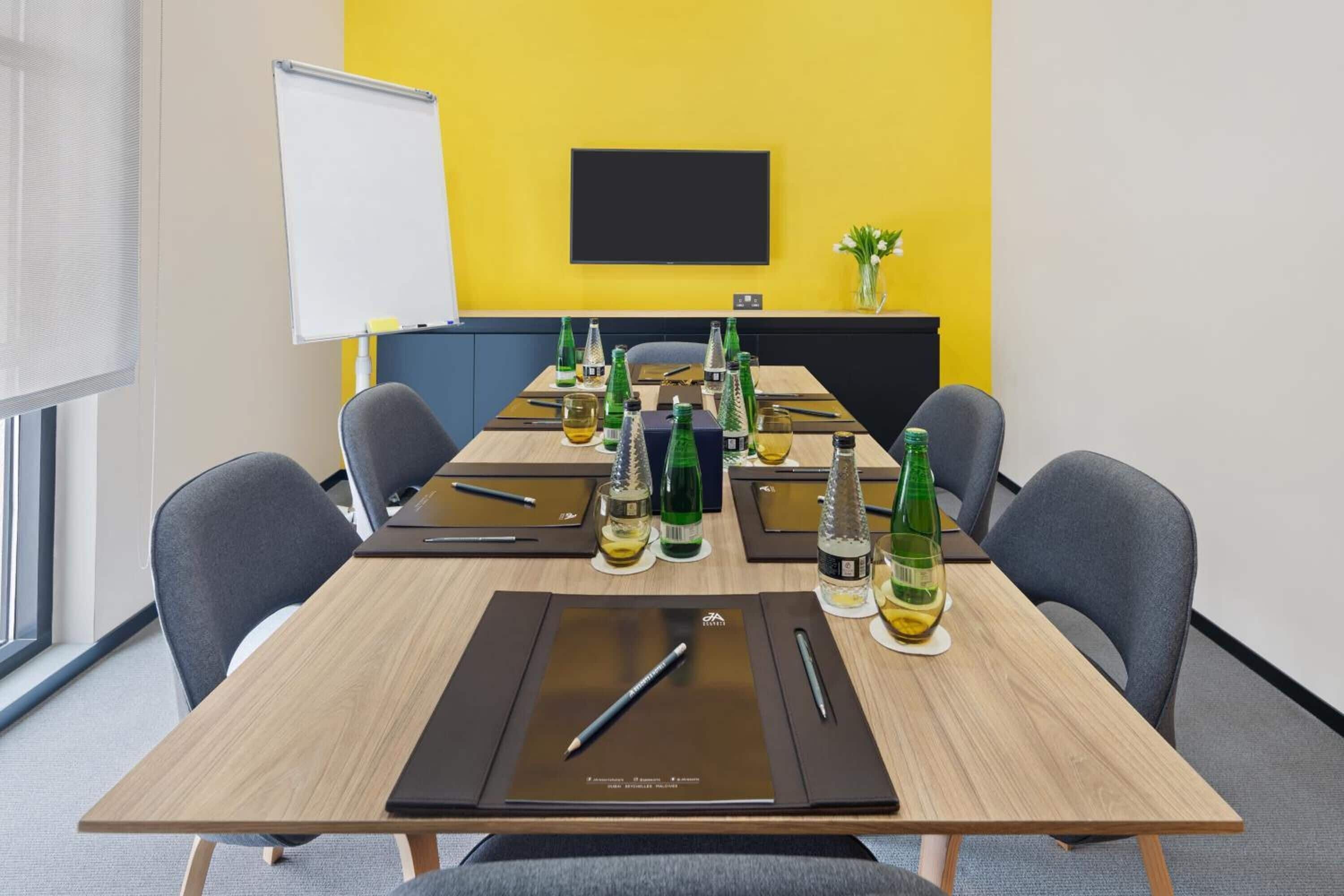 A conference room with a long table, chairs, a whiteboard, and a TV screen.