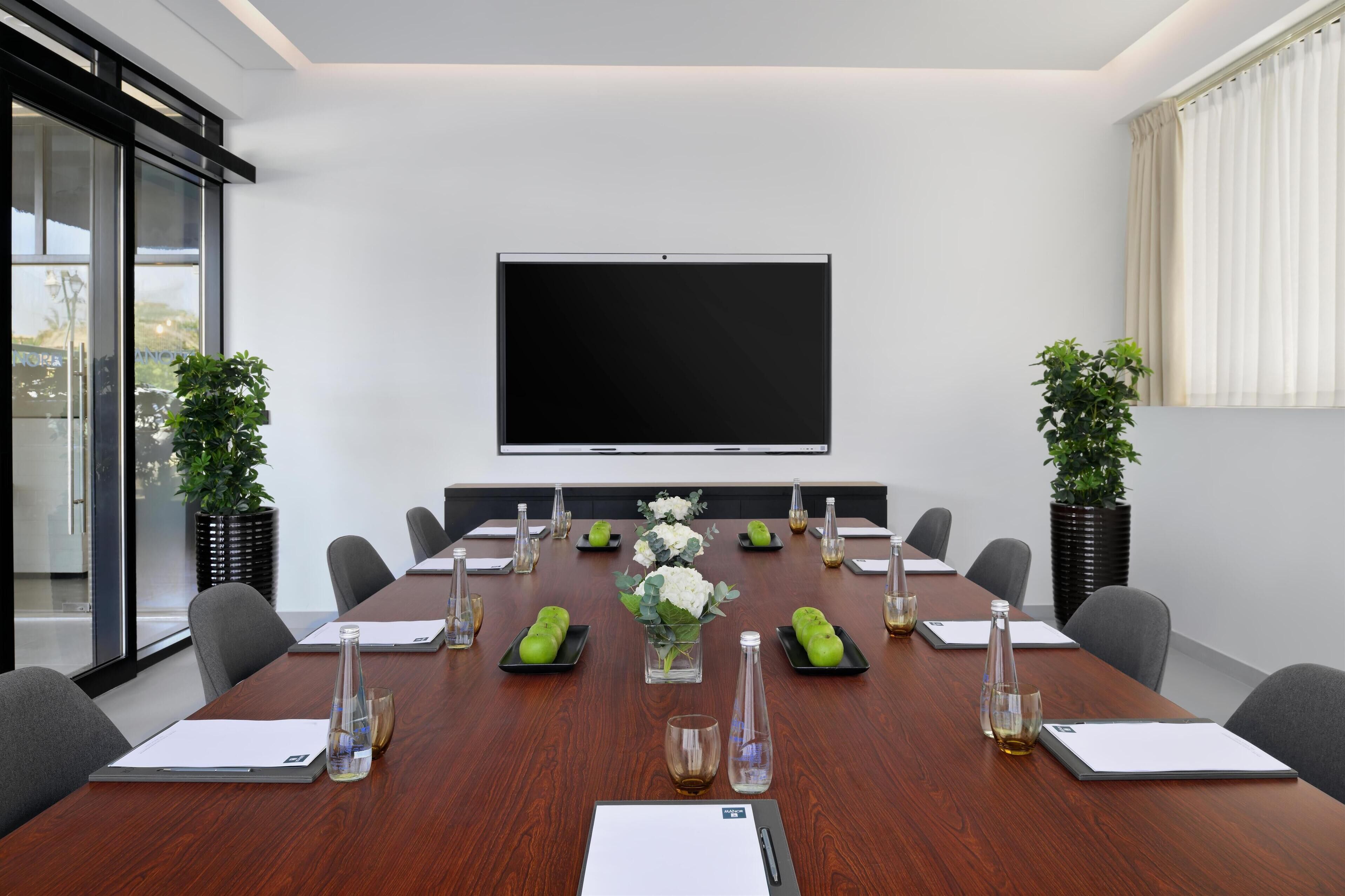 A conference room with a large table, chairs, a projector screen, and potted plants.