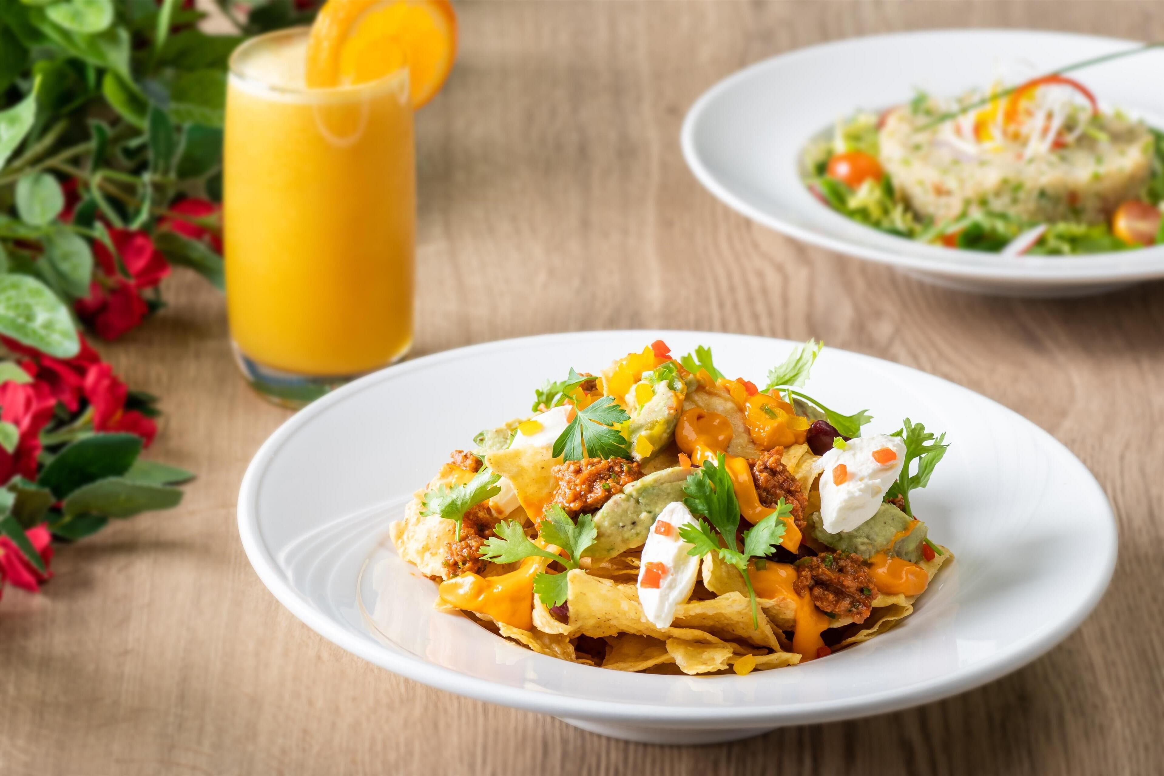 Nachos topped with cheese, sour cream, and guacamole on a white plate.