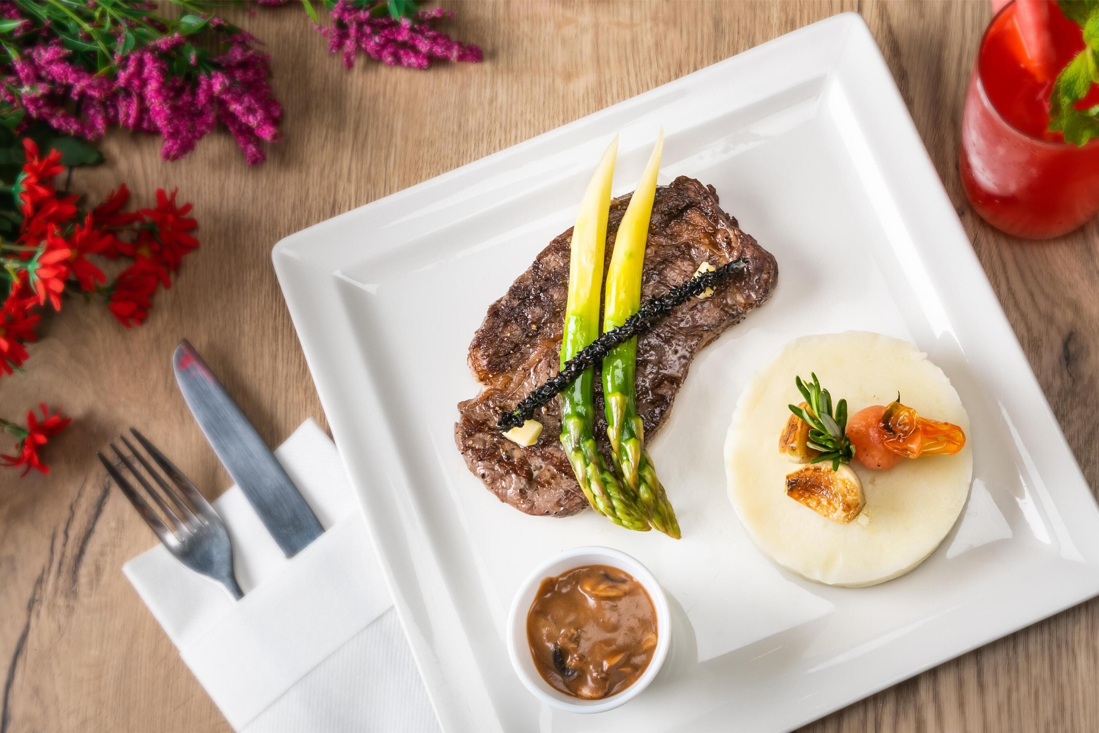 Une assiette blanche avec un steak, des asperges et un petit ramequin de sauce.