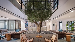 A spacious lobby with a large tree, leather sofas, wooden chairs, and a small table. - JA The Manor Hotel, Dubai (Dubai)