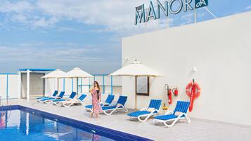 Zona de piscina de un hotel con sillones de descanso y sombrillas, un puesto de socorrista y un cartel que dice "The Manor Hotel".