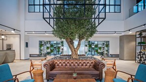 A spacious lobby with a large tree, leather sofa, and wooden coffee table. - JA The Manor Hotel, Dubai (Dubai)