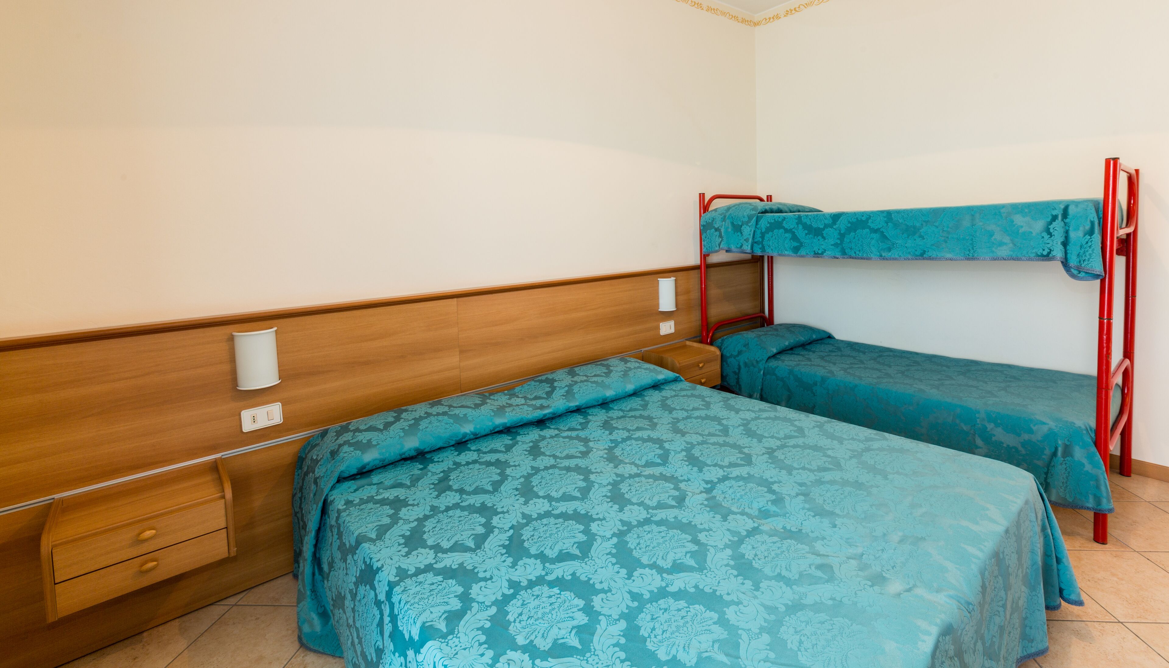 A room with two bunk beds, a wooden dresser, and a wall-mounted light fixture.