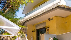 A residential building with a covered porch, a statue, and a small garden area. - Residence California (Jesolo)