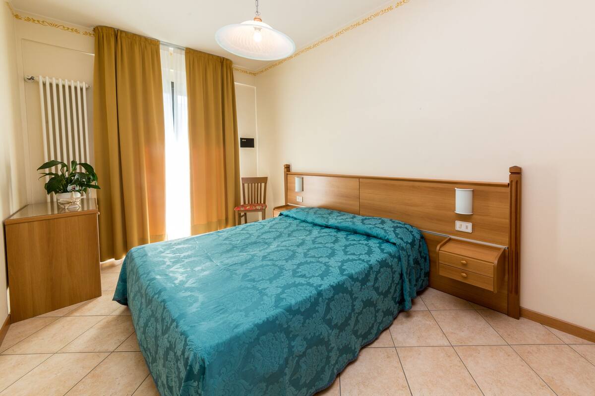 Une chambre à coucher comprenant un lit, des tables de chevet, une commode, une chaise, un radiateur et une plante en pot.