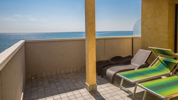 A balcony with two lounge chairs and a table, overlooking a clear blue sea. - Residence California (Jesolo)