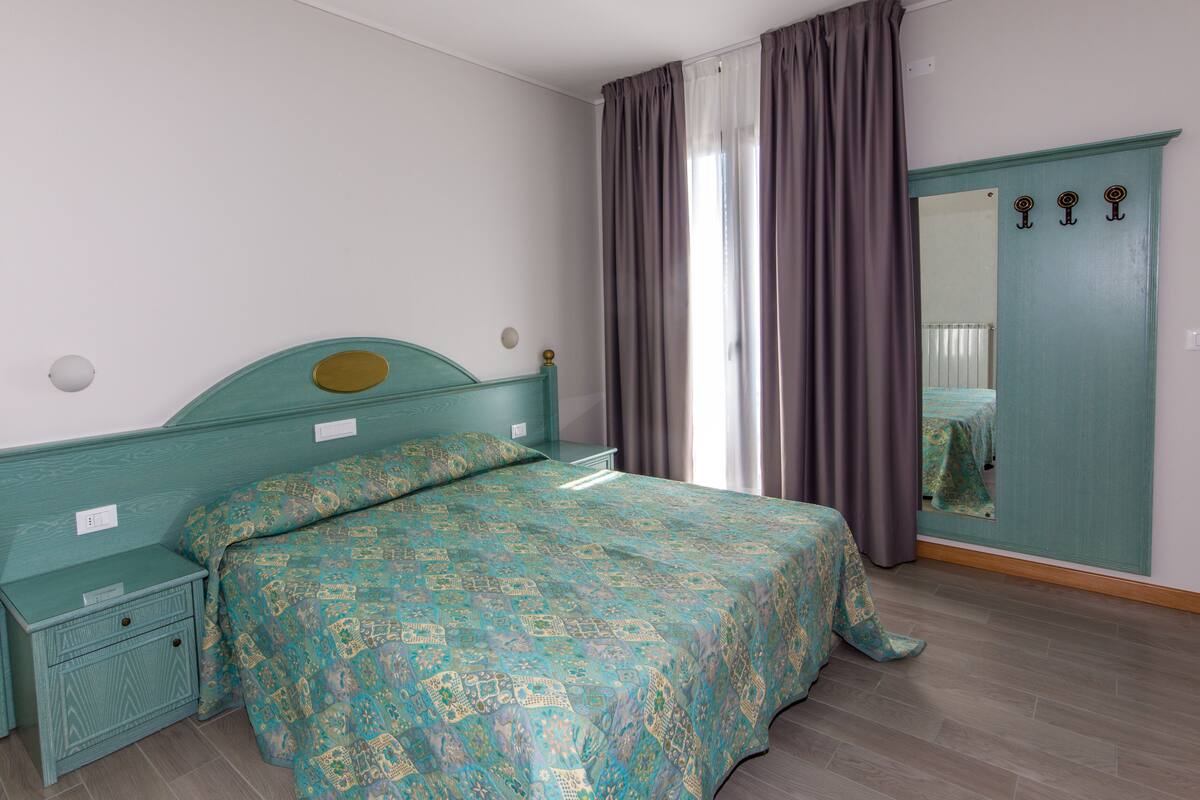 Une chambre à coucher comprenant un lit, une table de chevet, une commode, un miroir et une porte avec un porte-manteau.