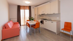 A compact living space with a kitchenette, a dining area with a table and chairs, and a sofa. - Residence California (Jesolo)