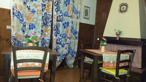 A dining area with wooden chairs and tables, a floral curtain, and a small potted plant on the table. - B&B Della Ciociaria (Ceprano)