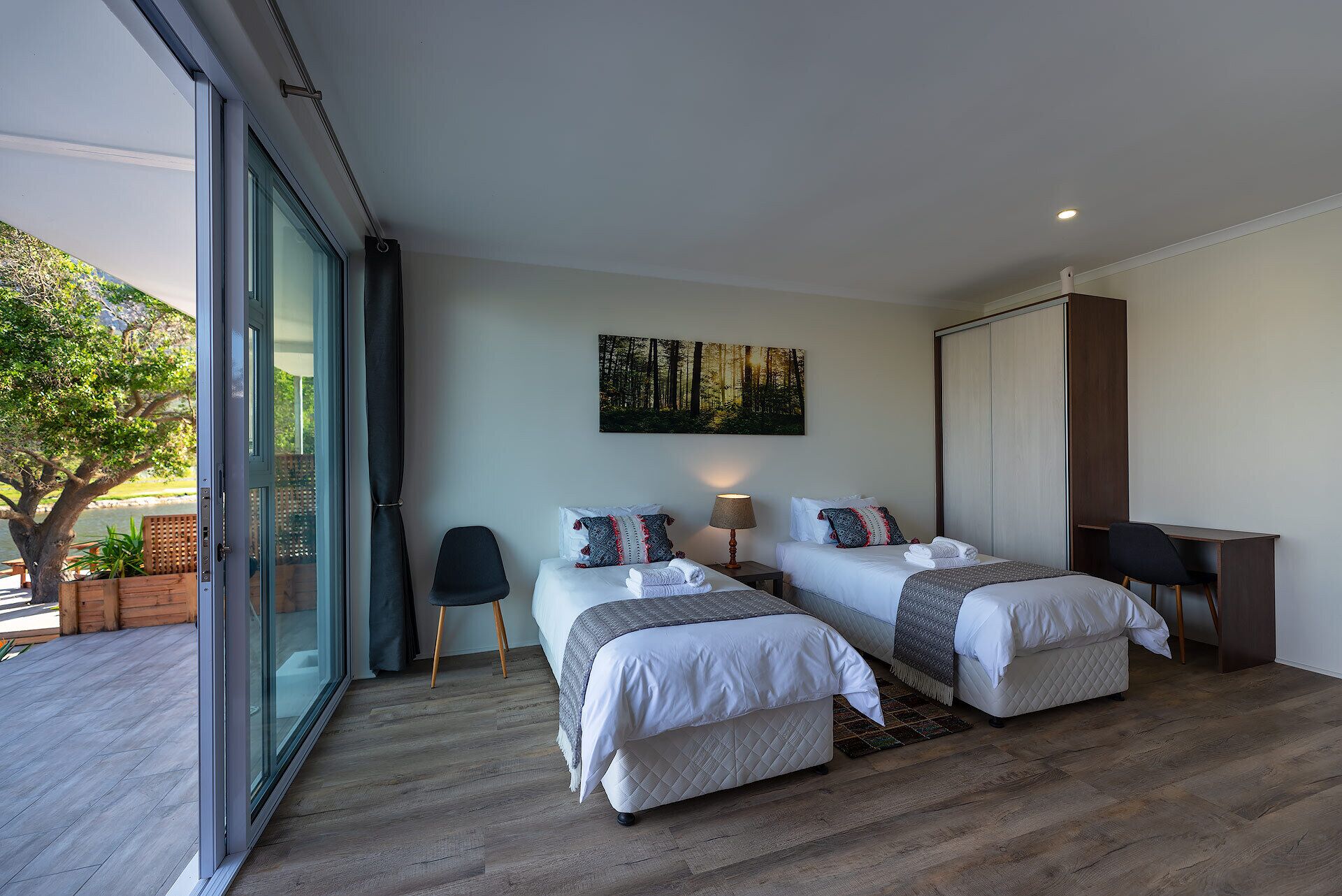 A modern bedroom with two beds, a desk, and a large window.