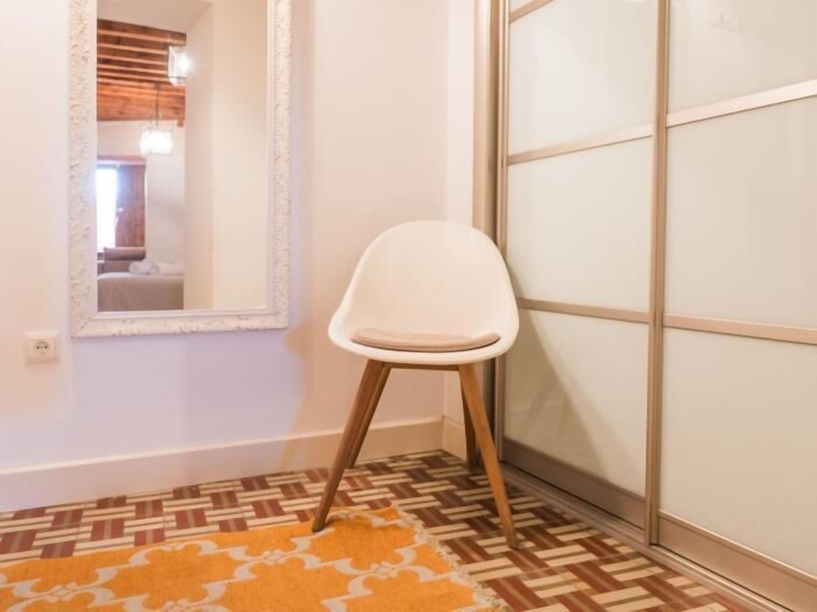 A room with a patterned floor, a white chair, and a mirror with a decorative frame.