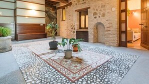 Une cour avec un sol à motifs, des murs en pierre, des poutres en bois et des plantes en pot.