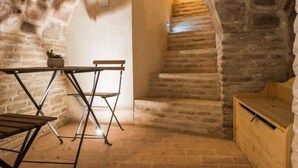 Une pièce aux murs de pierre, avec une table et des chaises en bois, une petite plante et un banc en bois.