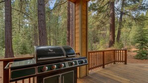 Ett trädäck med en inbyggd grillplats, omgivet av ett skogslandskap.