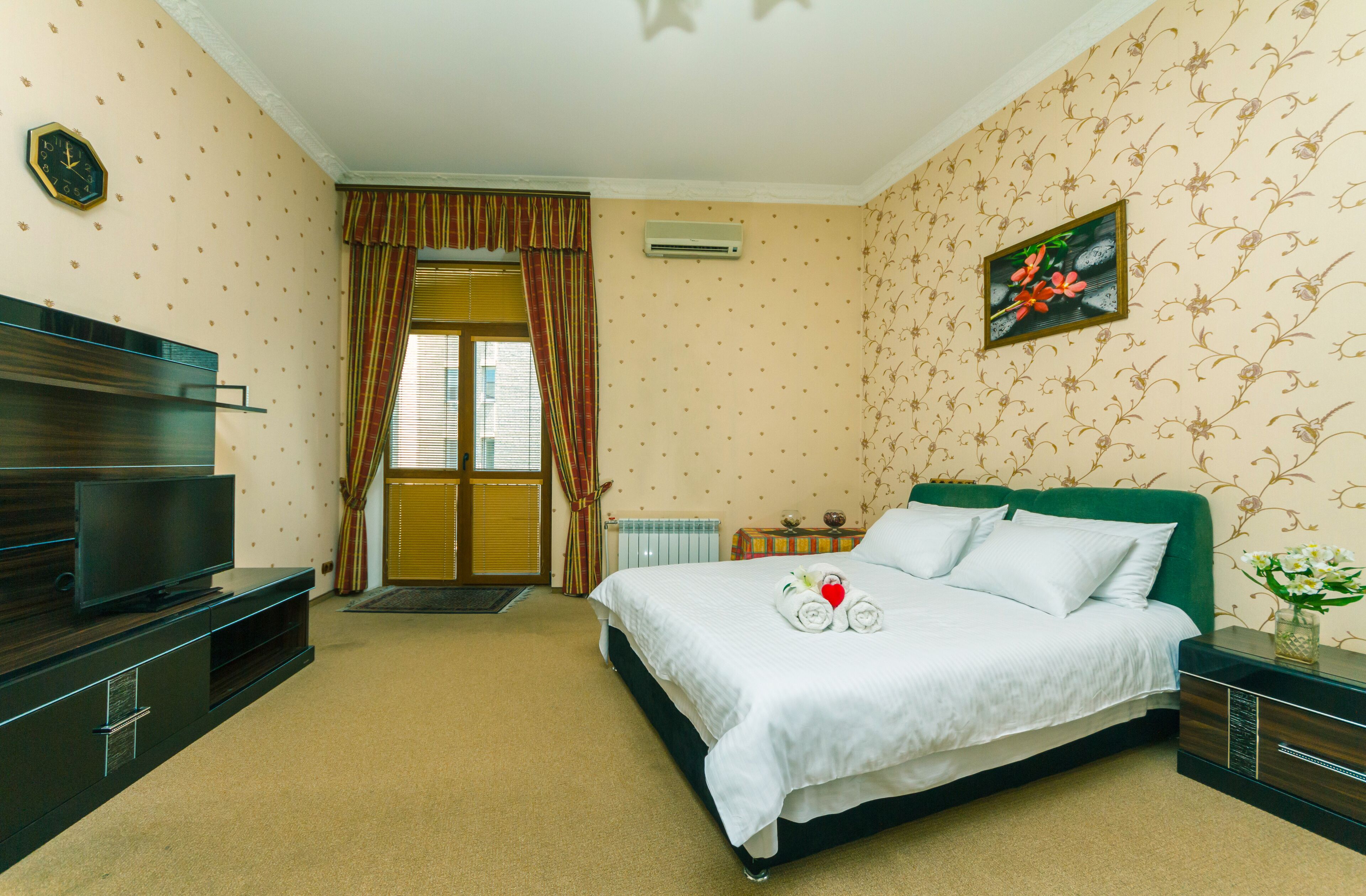 A hotel room with a bed, a TV, a radiator, and a window with curtains.