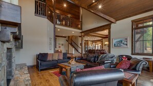 A spacious living room with a stone fireplace, leather sofas, and a wooden staircase leading to an upper level.