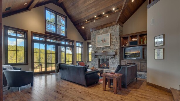 A spacious living room with a stone fireplace, large windows, and wooden flooring.