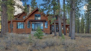 A two-story log cabin with a stone foundation, large windows, and a wooden porch.