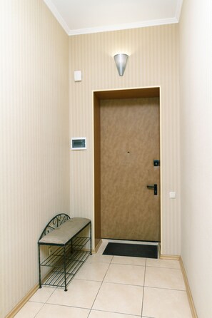 Un couloir avec une porte, un banc, un luminaire et un interrupteur fixé au mur.