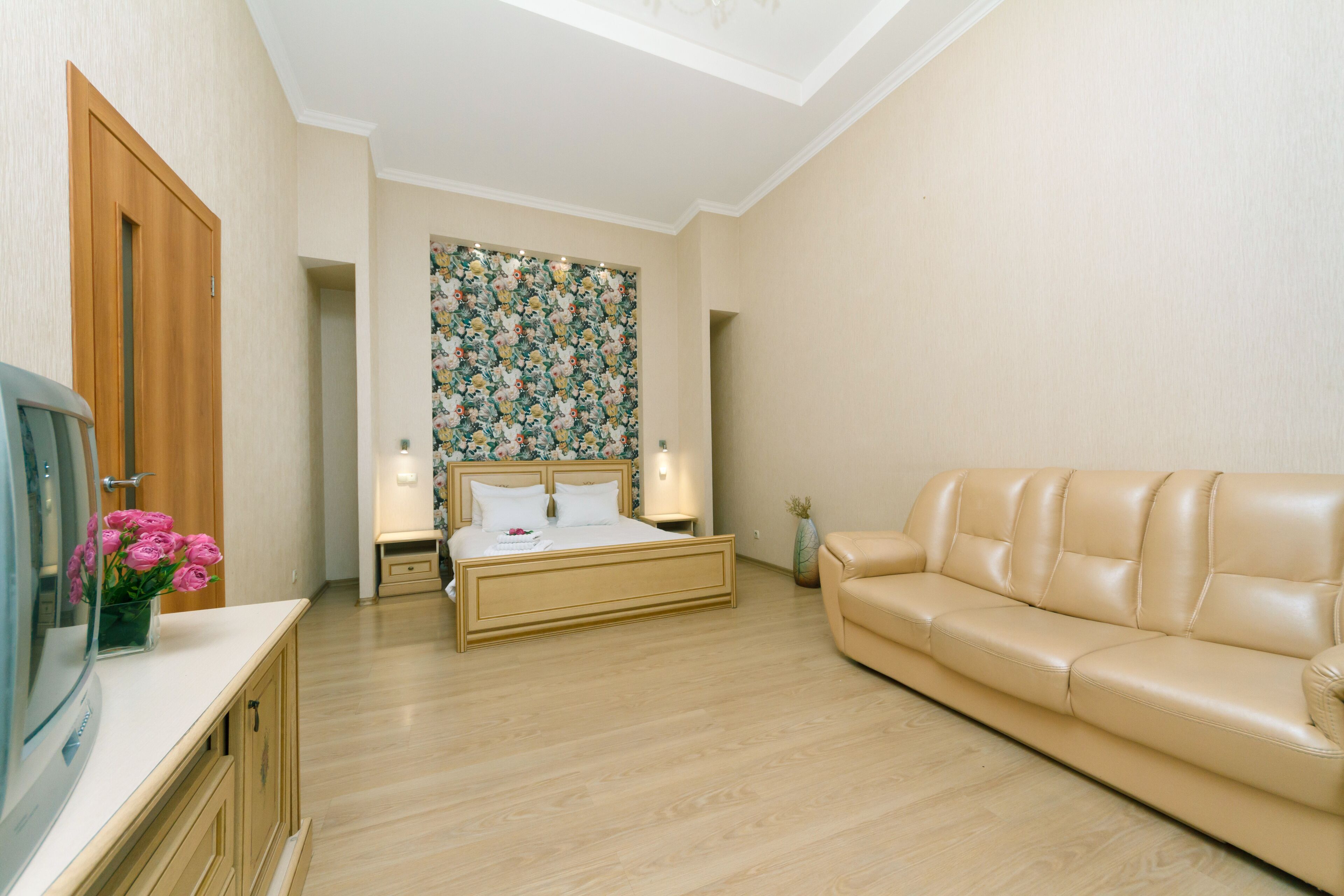 A bedroom with a bed, a sofa, a TV, and a floral wallpaper.