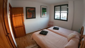 Ein Schlafzimmer mit zwei Betten, einem Holzschrank, einem Fenster mit Jalousien und zwei gerahmten Bildern an der Wand.