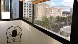 Ein Balkon mit Blick auf ein mehrstöckiges Gebäude, einem Stuhl und einem Fenster mit Rollläden.