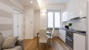 A modern kitchen with white cabinets, a dining table, and chairs. - BnButler - Friuli, 24 (Milano)