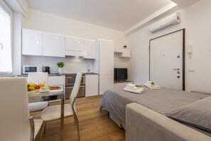 A modern hotel room with a bed, a desk with a chair, a kitchenette, and a TV. - BnButler - Friuli, 24 (Milano)