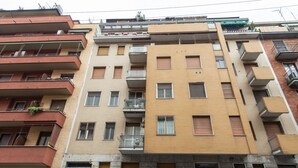 A multi-story residential building with balconies, a visible ground-floor business, and a sign indicating a car rental service. - BnButler - Friuli, 24 (Milano)
