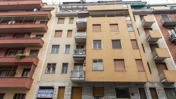 Un edificio residenziale a più piani con balconi, un'attività commerciale al piano terra e un cartello che indica un servizio di autonoleggio.
