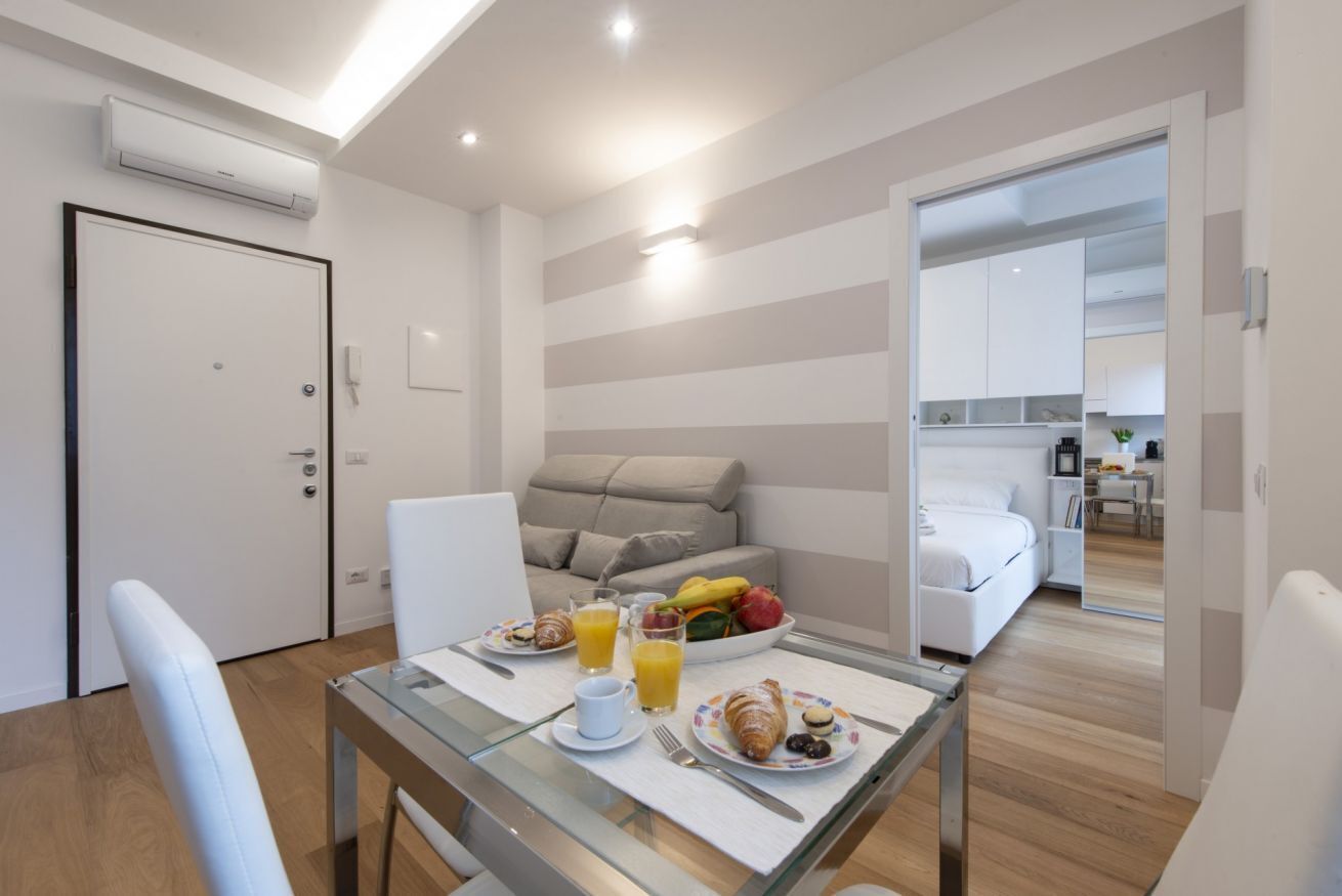 Een moderne hotelkamer met een zithoek, een bank, een bed en een keuken op de achtergrond.