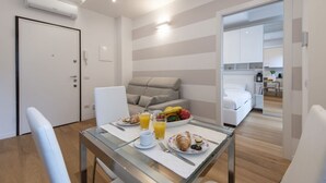 A modern hotel room with a dining area, a sofa, a bed, and a kitchen in the background. - BnButler - Friuli, 24 (Milano)