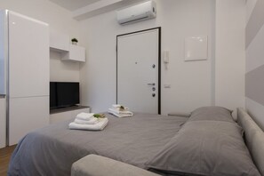 A modern hotel room with a bed, a TV, a door, and an air conditioning unit.