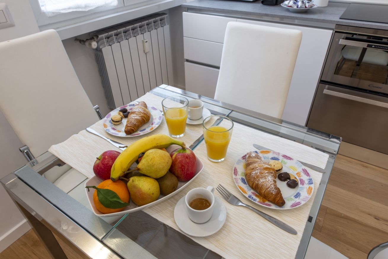 A breakfast table with fruits, croissants, and juice in a modern kitchen.