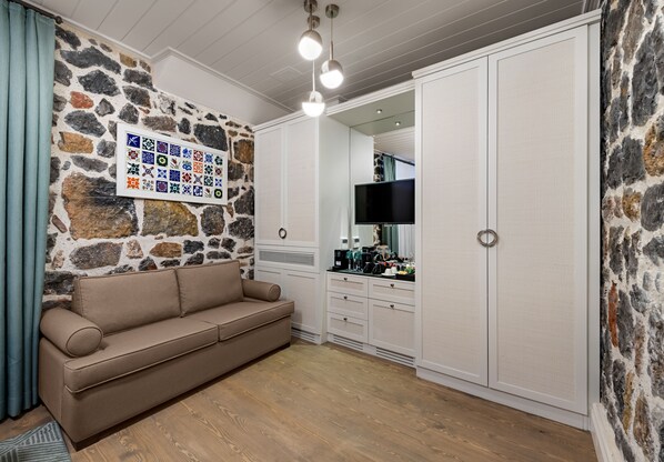 A living room with a stone wall, a beige sofa, a flat-screen TV, and a wardrobe. - Catch Sultanahmet - Special Class (Istanbul)