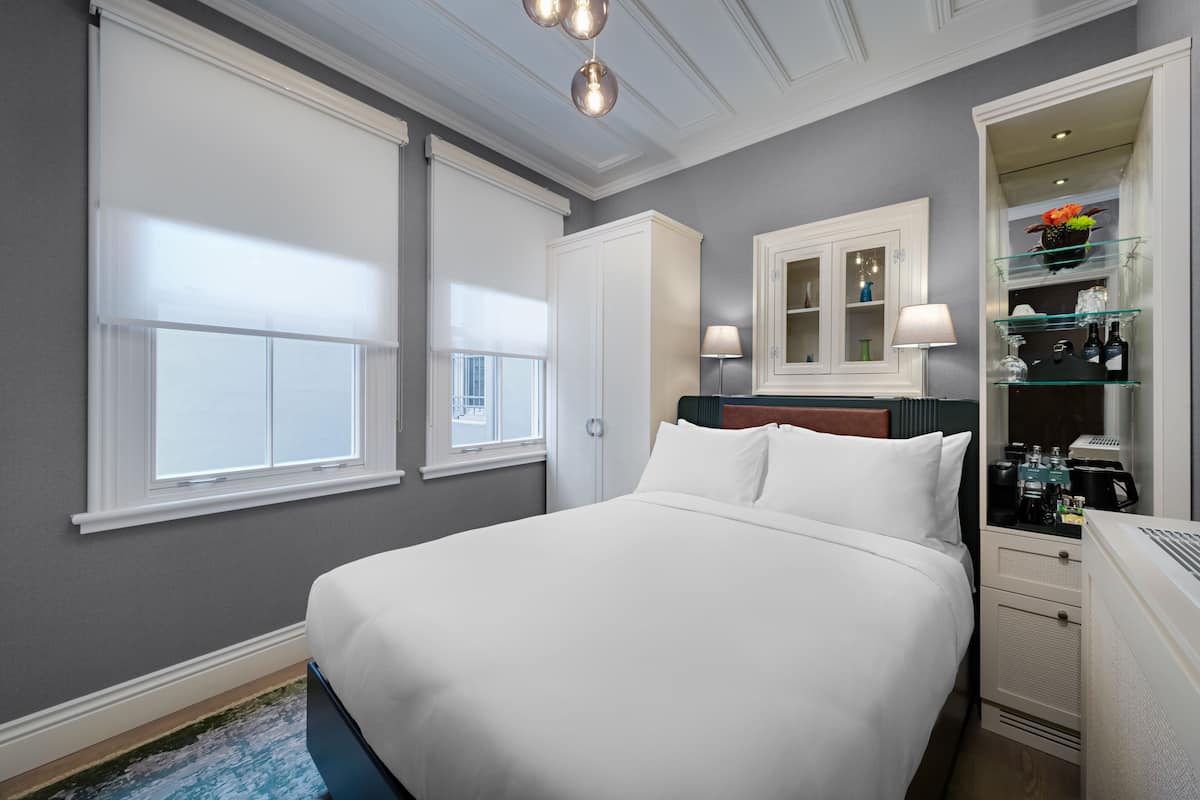 A hotel room with a large bed, a wardrobe, a vanity with a mirror, and a shelf with toiletries.