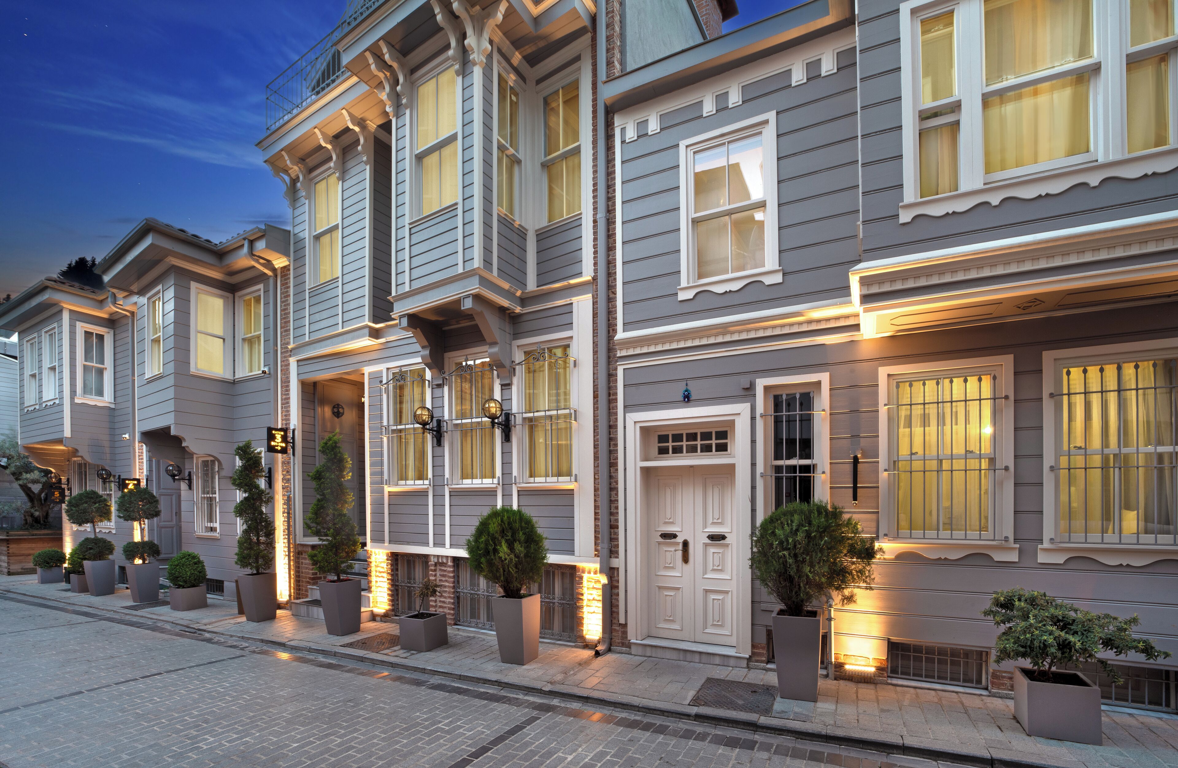 A row of traditional-style townhouses with uniform architecture, large windows, and outdoor lighting.
