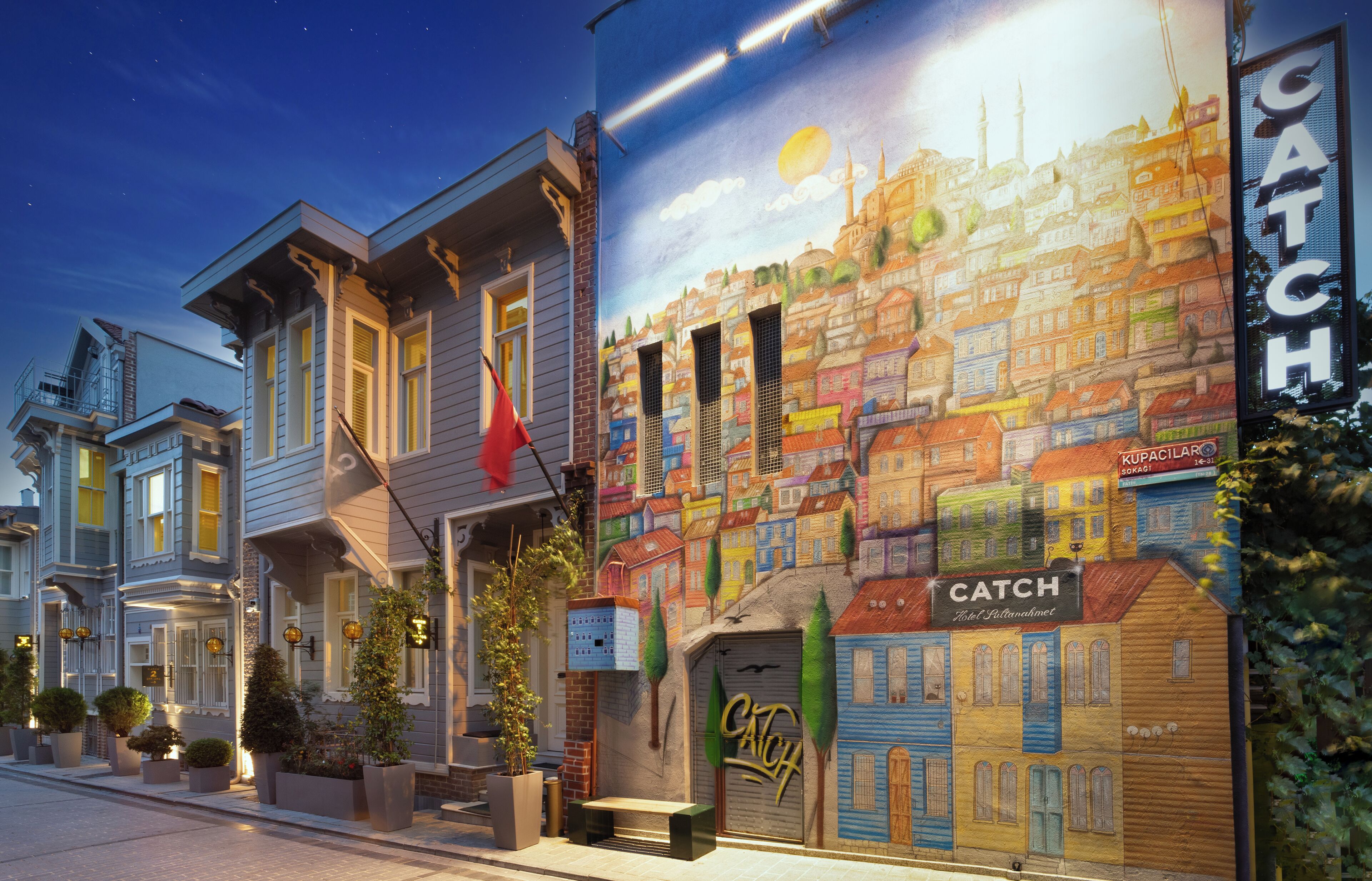 A hotel facade with a mural of a cityscape, a prominent 'CATCH' sign, and a 'TRUCILAR' sign indicating a restaurant.