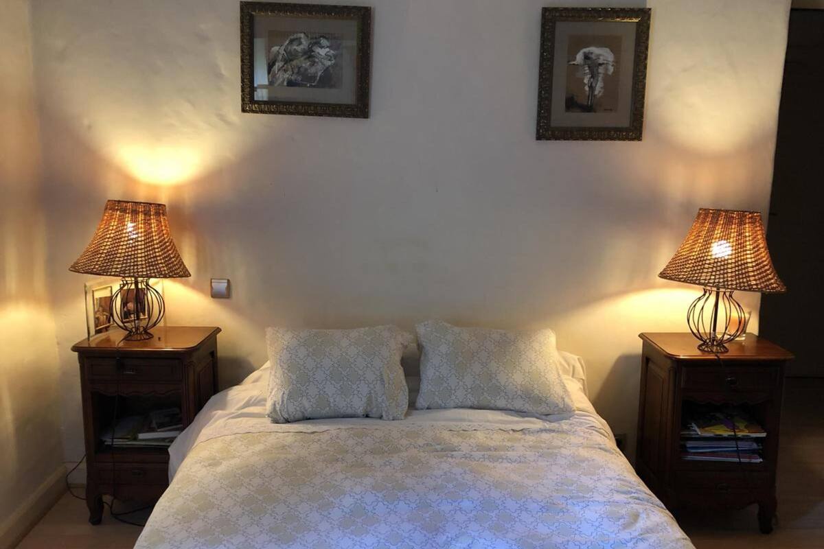 Une chambre à coucher comprenant un lit, deux tables de chevet, deux lampes et deux tableaux encadrés accrochés au mur.