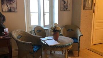 Une pièce avec une table ronde, deux chaises en osier dotées de coussins bleus, un vase avec des fleurs et des œuvres d’art accrochées aux murs.