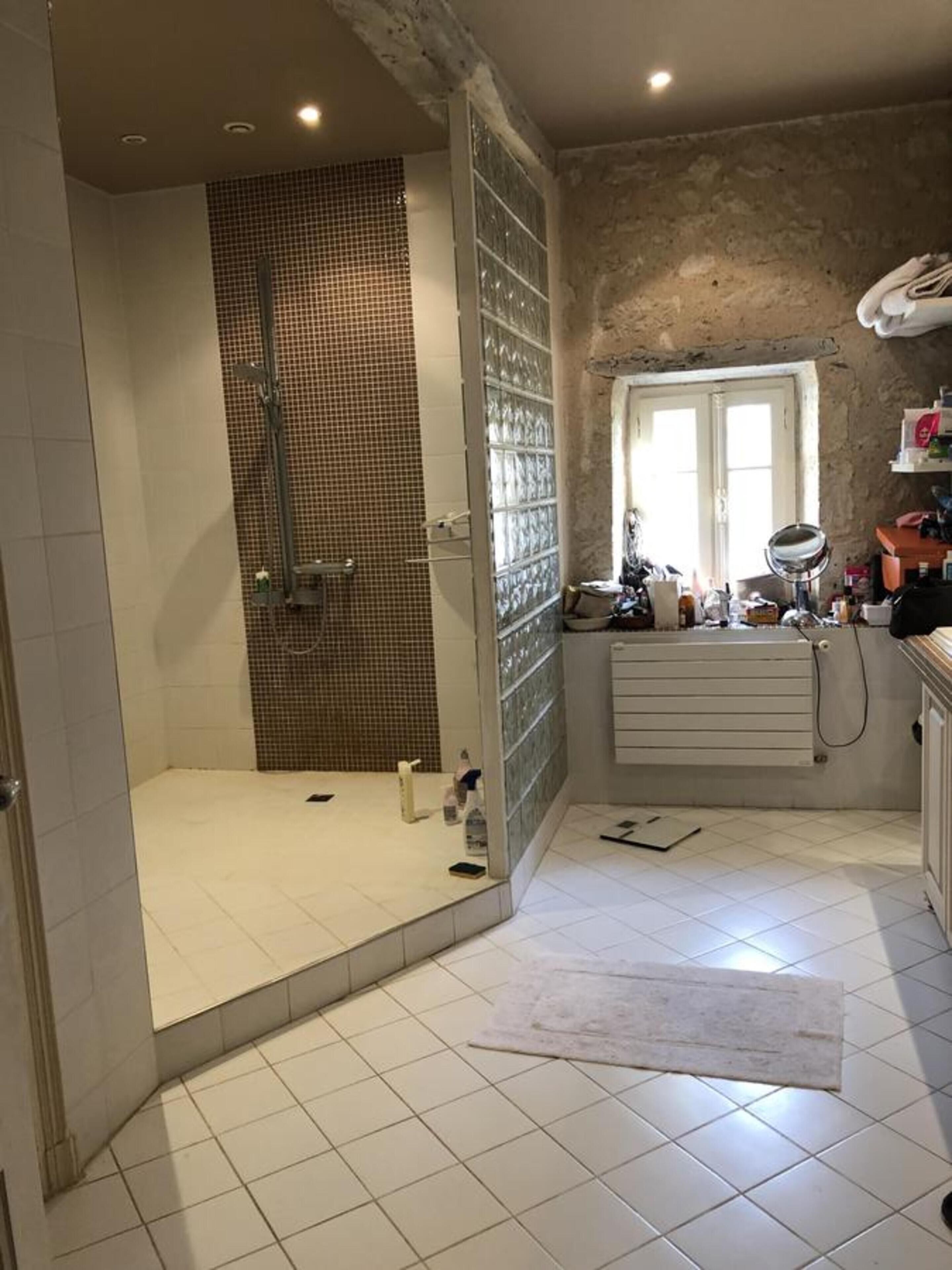 Baño con ducha, paredes de azulejos, radiador y ventana.