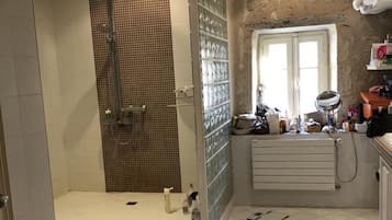 Baño con ducha, paredes de azulejos, radiador y ventana.