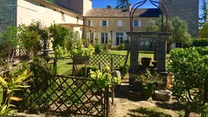 A courtyard with a stone fountain, a pergola, and a garden with various plants. - Chambres d'Hotes Las Caneres (Castelnau-d'Arbieu)
