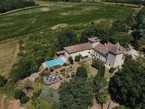 Vue aérienne d’un vaste domaine comprenant une piscine, un espace de détente extérieur et un bâtiment en pierre doté de plusieurs tours.