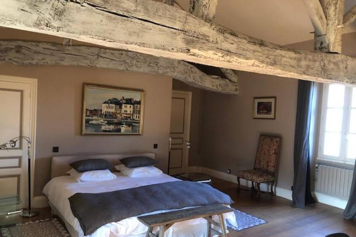 Une chambre avec un grand lit, une chaise, un tableau et une fenêtre.