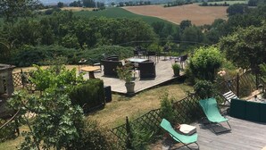 A deck with outdoor furniture, surrounded by lush greenery and a view of rolling hills. - Chambres d'Hotes Las Caneres (Castelnau-d'Arbieu)