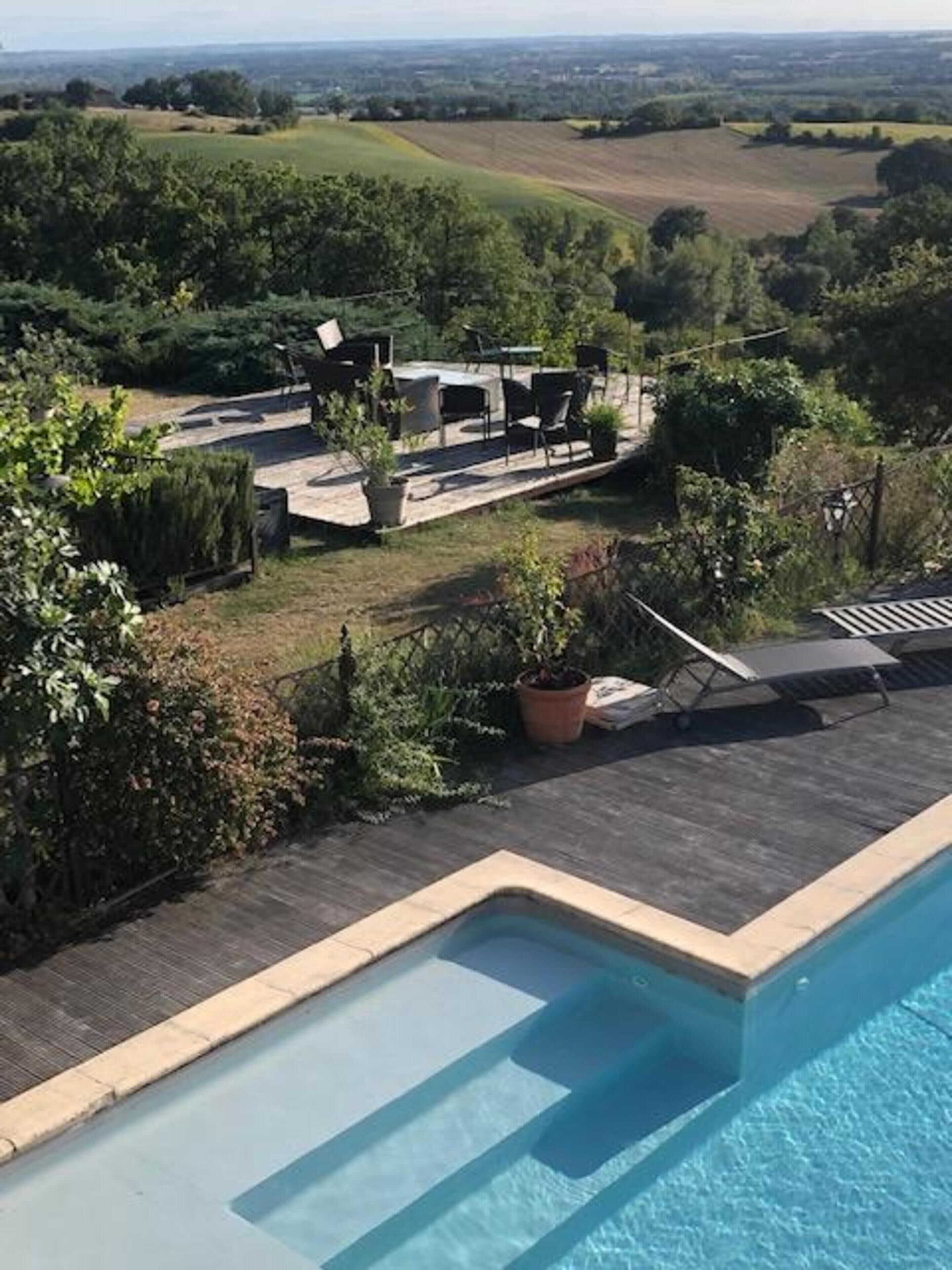 Ein Schwimmbecken mit Liegefläche, umgeben von Grün und Blick auf die Landschaft.