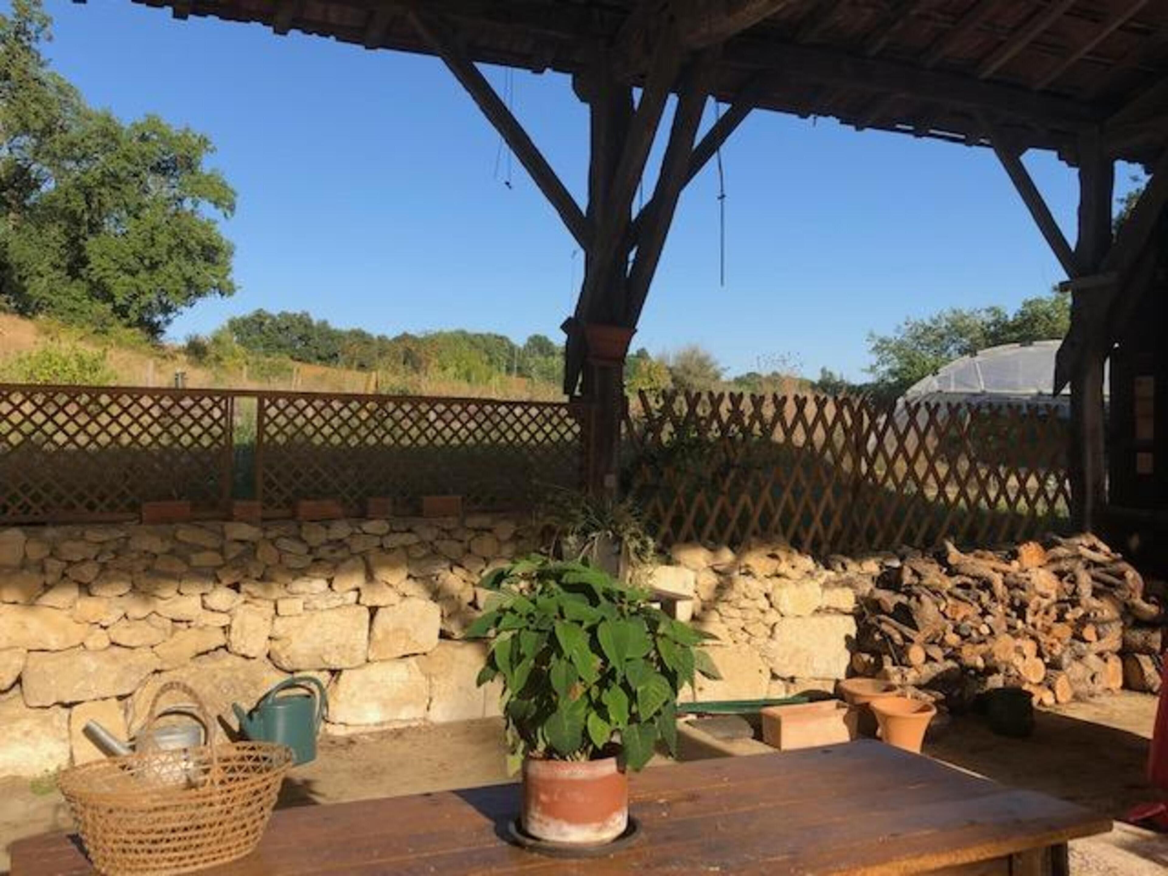 Un décor extérieur rustique agrémenté d’un mur en pierre, d’une table en bois, d’une plante en pot et d’un panier.