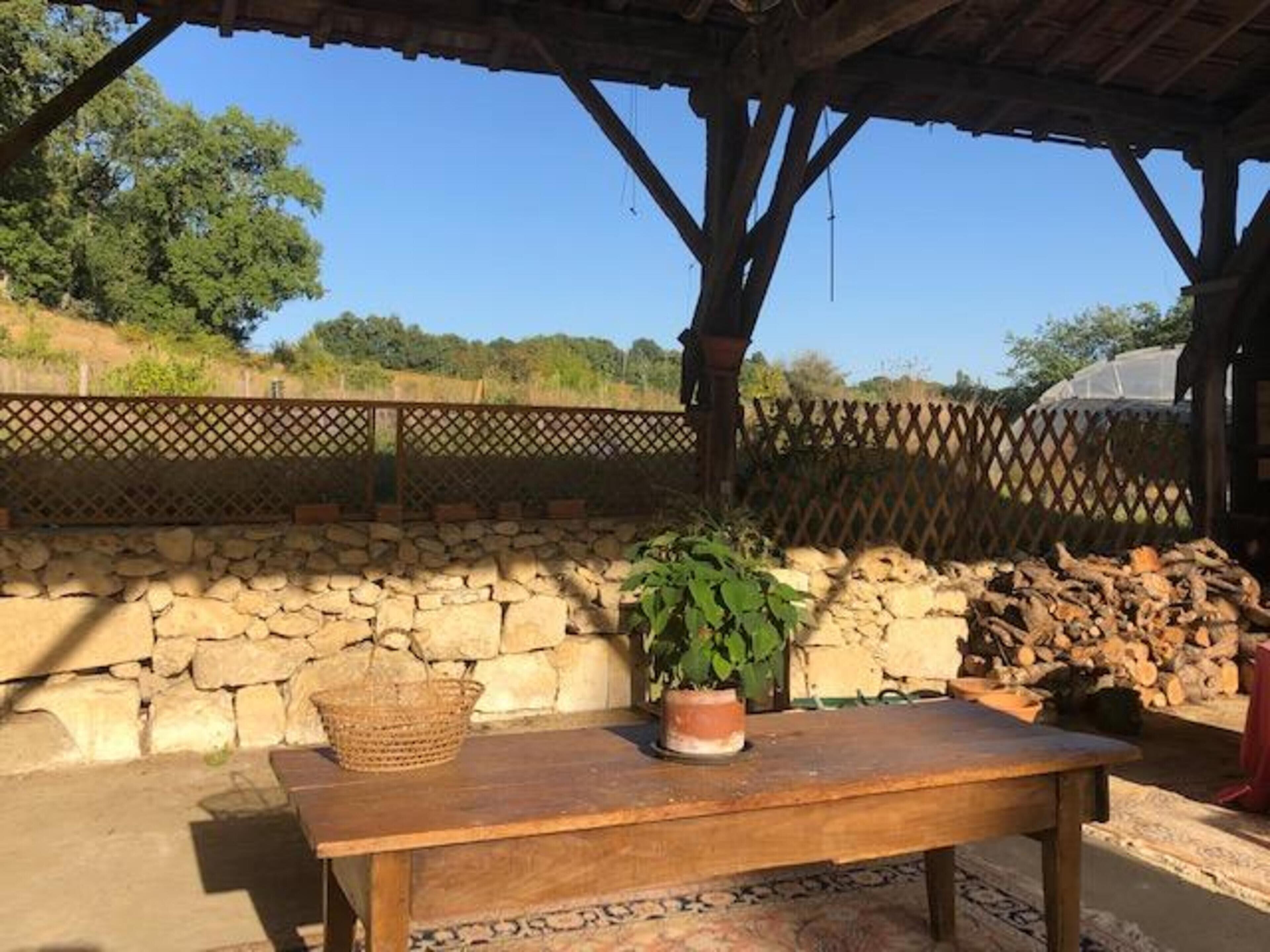 A rustic outdoor seating area with a stone wall, a wooden table, a woven basket, and a potted plant.